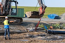 Der Moment des landseitigen Kabel-Austritts aus dem Leerrohr: Ein Bagger unterstützt die Zugkraft der Winde beim Seekabeleinzug von NordLink unter dem Büsumer Deich hindurch.